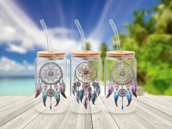 Glasbecher mit Bambusdeckel und Glastrinkhalm, verziert mit einem detaillierten Traumfänger-Motiv in sanften Farben. Der Traumfänger ist mit Federn und Perlen dekoriert und verleiht dem Becher eine mystische und natürliche Ausstrahlung. Der Becher steht v